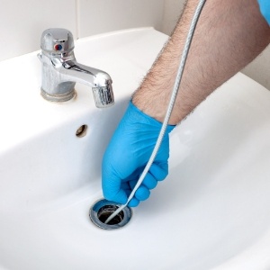 man wearing blue gloves cleaning a drain
